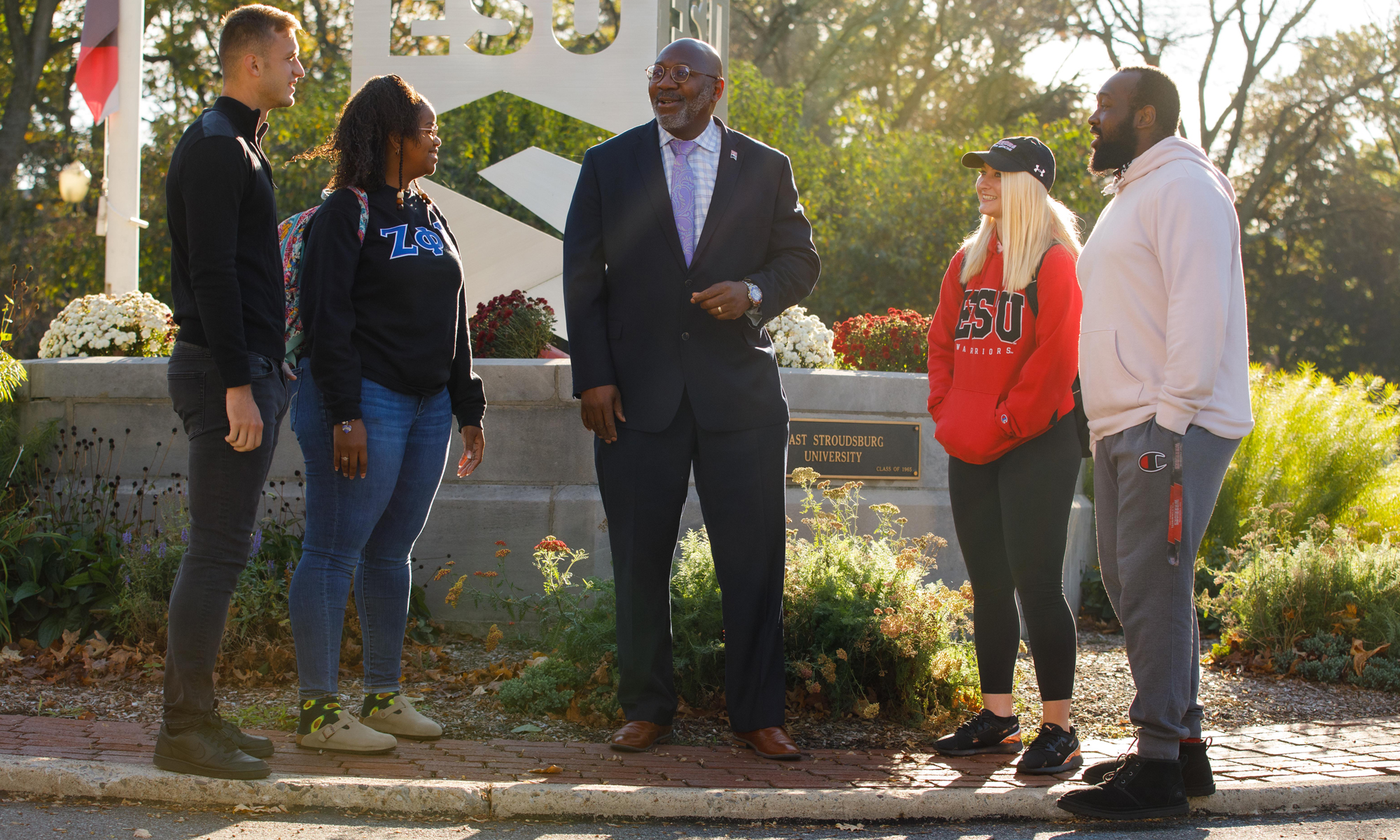 ESU's president talks with four students near an "ESU" sign on campus.