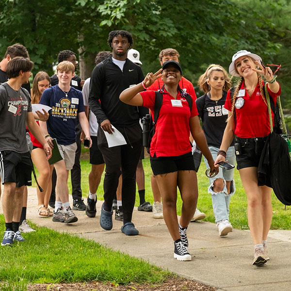 A group of students walking on campus, with two in red shirts making peace signs.